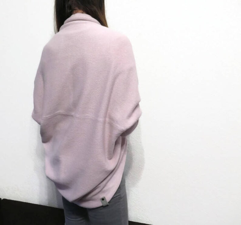 May include: A soft, pale pink, oversized sweater with a draped design. The sweater is made of a fuzzy, knit fabric.