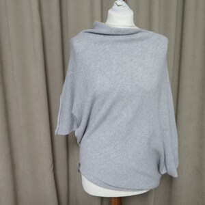 May include: A gray knitted sweater with a cowl neck and a loose fit.