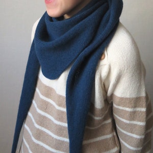 Könnte beinhalten: Eine Person trägt einen gestreiften Pullover mit einem langen, dunkelblauen Schal. Der Schal ist um den Hals gebunden und hängt an der Vorderseite des Pullovers herunter.