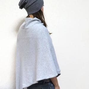 May include: A light gray knitted poncho with a slouchy gray beanie. The poncho has a cowl neck and is worn over a pair of blue jeans.