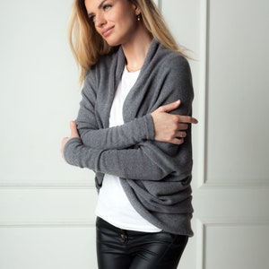 May include: A woman wearing a gray cashmere cardigan over a white t-shirt and black leather pants.