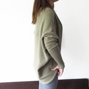 May include: A loose-fitting, light green sweater with long sleeves. The sweater is made of a soft, knitted fabric and has a draped, relaxed fit.
