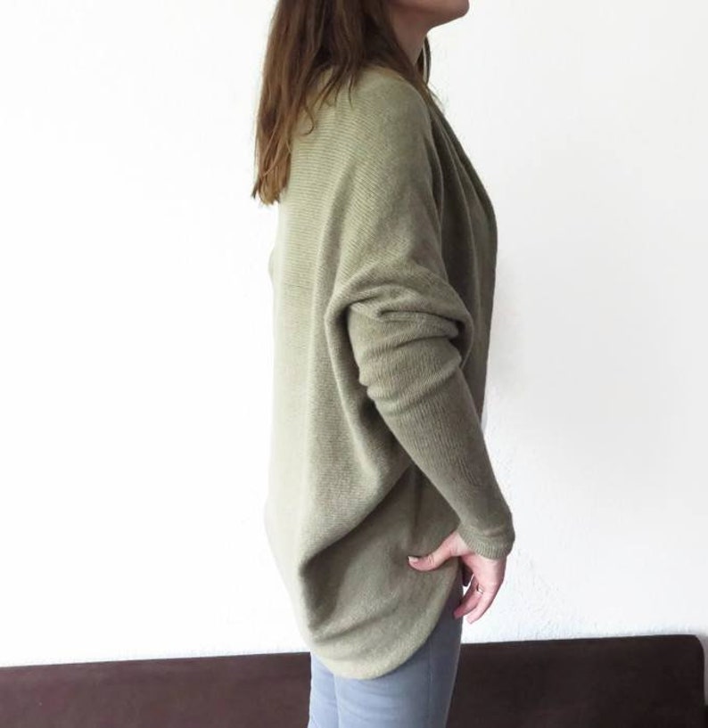 May include: A loose-fitting, light green sweater with long sleeves. The sweater is made of a soft, knitted fabric and has a draped, relaxed fit.