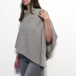 May include: A gray knitted poncho with a cowl neck. The poncho is draped over a person's shoulders and is made of a soft, comfortable fabric.