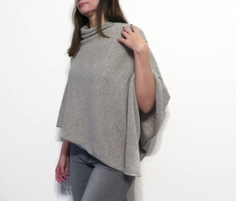 May include: A gray knitted poncho with a cowl neck. The poncho is draped over a person's shoulders and is made of a soft, comfortable fabric.