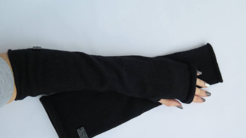 May include: A pair of black fingerless gloves made of a soft, knitted fabric. The gloves are long and extend past the wrist.