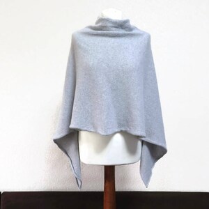 May include: A light gray knitted poncho with a cowl neck and a triangular shape.