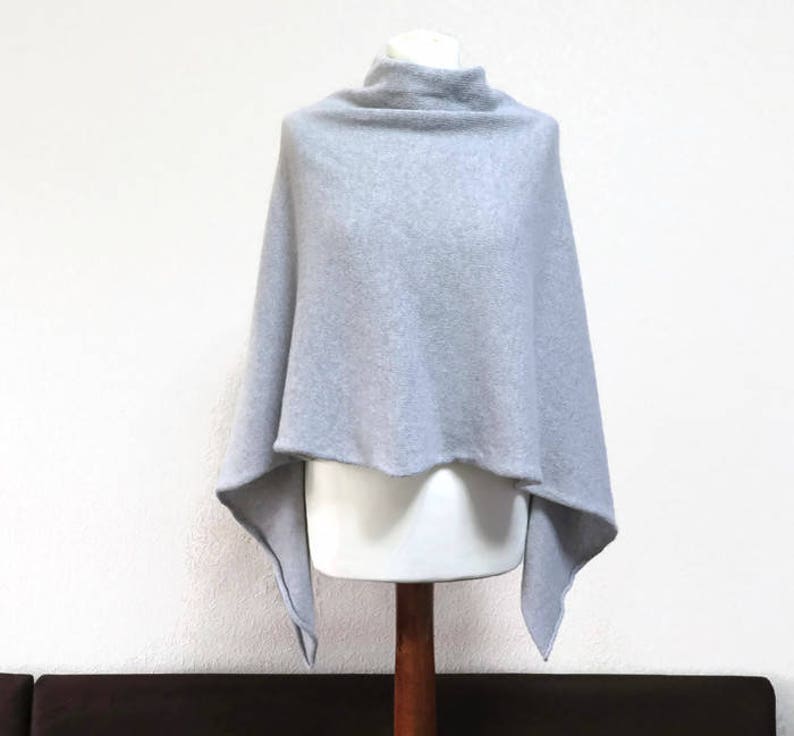 May include: A light gray knitted poncho with a cowl neck and a triangular shape.