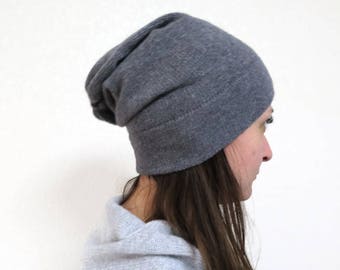 May include: A charcoal grey slouchy beanie hat made of a fine-knit fabric. The hat features a relaxed, elongated fit that drapes toward the back of the head, providing a soft texture and a consistent solid color throughout the entire garment.