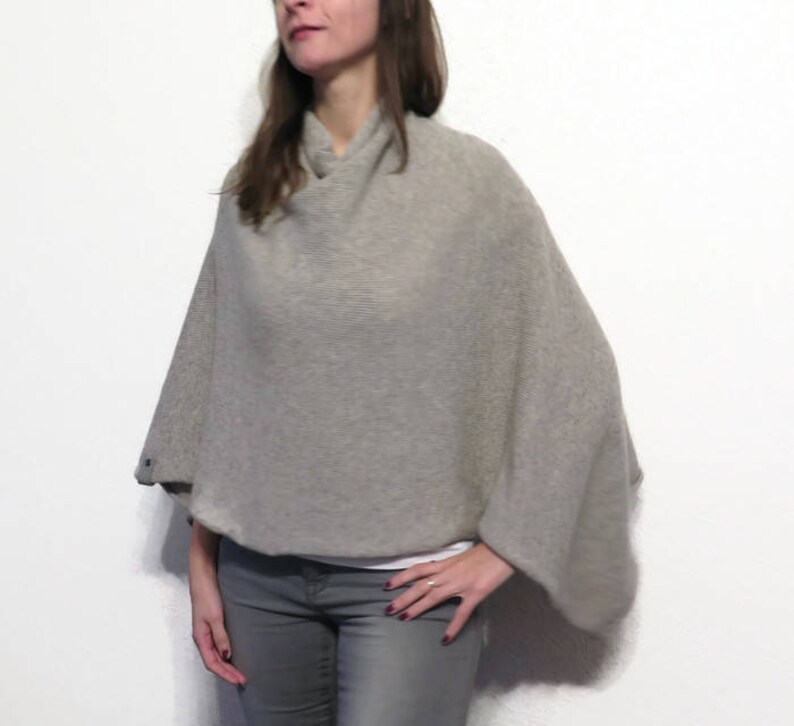 May include: A gray knitted poncho with a cowl neck and long sleeves. The poncho is made of a soft, lightweight fabric and is perfect for layering.