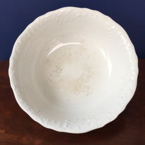 Könnte beinhalten: Weiße Keramikschüssel mit einem dekorativen, erhabenen Blumenmuster am Rand. Die Schüssel ist innen leicht abgeplatzt.