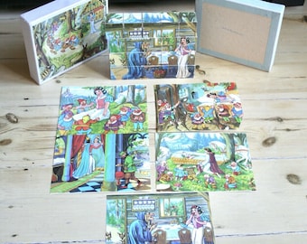 May include: A set of vintage Snow White wooden picture blocks featuring colorful illustrations of characters from the story. The set includes a white storage box, a light blue lid, and several printed cards showing the completed scenes.