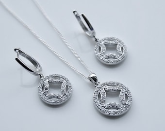 May include: A silver necklace and earrings set with a circular pendant and matching earrings. The pendant and earrings feature a geometric design with a square shape in the center, surrounded by smaller circles of sparkling stones.