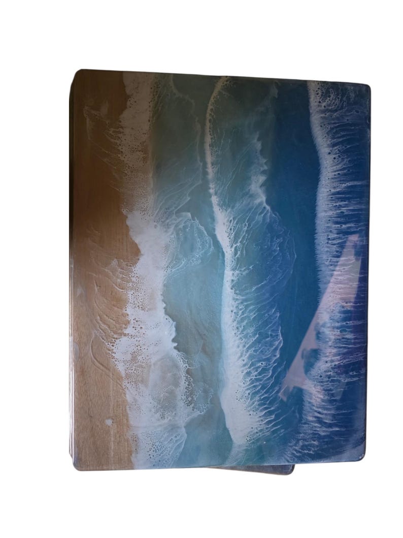 May include: A rectangular wooden serving tray with a resin ocean wave design. The tray features a sandy beach on the left, transitioning to foamy white waves and deep blue ocean on the right. The resin gives a glossy finish.