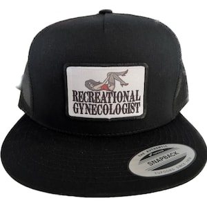 May include: Black trucker cap with a flat peak and mesh back. The front displays a rectangular patch with the text "RECREATIONAL GYNECOLOGIST" and an illustration of a woman in lingerie.