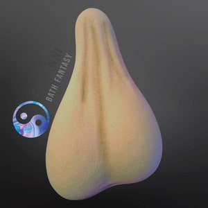 May include: A light yellow bath bomb shaped like a testicle. The bath bomb has a textured surface and is slightly iridescent.