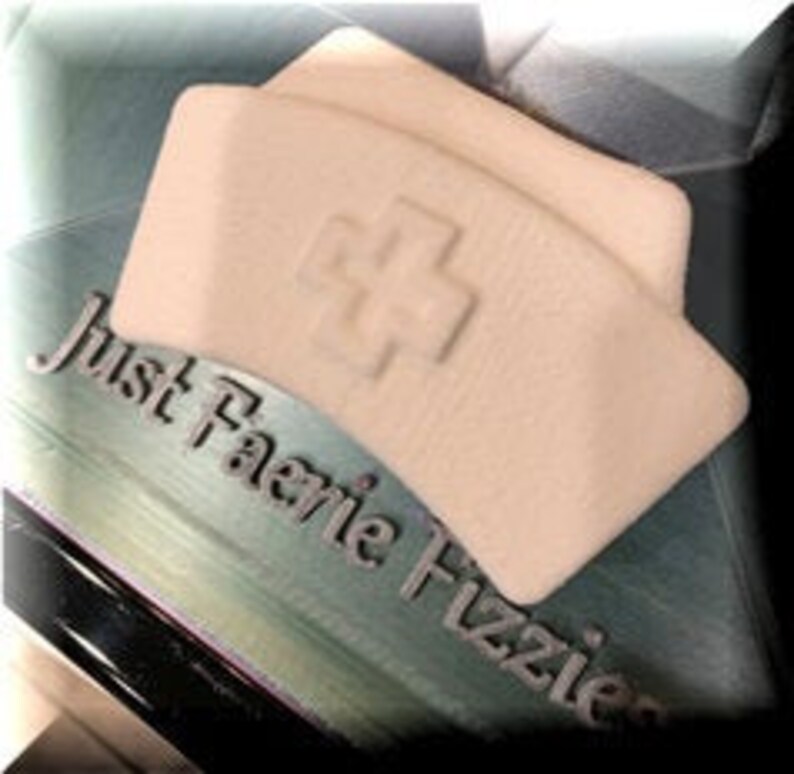May include: White nurse's hat with a red cross on the front. The hat is made of a soft, textured material. "Just Faerie Fizzies" is written on the background.