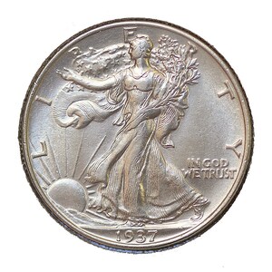 May include: A silver Walking Liberty half dollar coin with the year 1937 inscribed on the bottom. The coin features a woman walking forward with a branch of laurel in her right hand and a branch of oak in her left hand. The inscription "IN GOD WE TRUST" is visible on the right side of the coin.