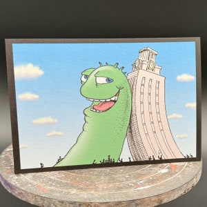 May include: A green cartoon monster with a wide smile and blue eyes stands next to a white building with a clock tower. The monster is holding the building up with its arm. There are small black figures in the foreground.