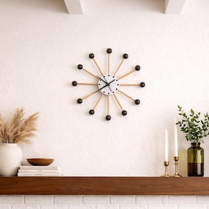 May include: A modern living room with a white brick fireplace, a wooden mantel, and a round coffee table. A starburst clock hangs above the fireplace. Decorative items include vases, candles, and a bowl of pinecones. A fire burns in the fireplace.