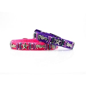 May include: Two decorative pet collars. One is hot pink, the other is purple. Both collars are embellished with silver-coloured seahorses and starfish, and colourful beads. The collars are designed for pets.