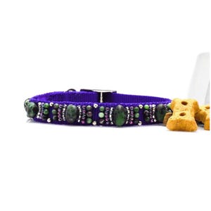 Puede incluir: Un collar morado para perros con detalles de cuentas verdes y plateadas. El collar presenta grandes piedras verdes ovaladas y cuentas más pequeñas. Se ve un cierre de metal plateado. Golosinas para perros en el fondo.