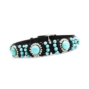 May include: A black macrame bracelet with turquoise and silver accents. The bracelet features three large turquoise stones surrounded by silver beads, with smaller turquoise beads and black macrame cord.