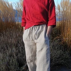 Può includere: Un paio di pantaloni di lino beige chiaro con vita a coulisse. I pantaloni sono a gamba larga e hanno una vestibilità rilassata.