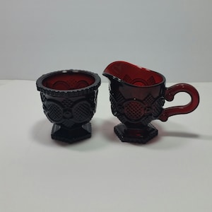 May include: A red glass creamer and sugar bowl set with a raised pattern. The set is made of ruby red glass and has a vintage look.