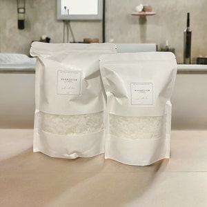 May include: Two white resealable bags filled with white magnesium flakes. The bags have labels that say "Magnesium Flakes" and "Bath Soak"
