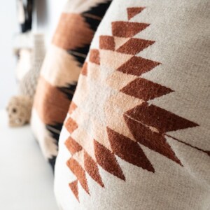 Puede incluir: Dos almohadas con patrones geom&eacute;tricos. La almohada en primer plano es beige con un dise&ntilde;o geom&eacute;trico marr&oacute;n y melocot&oacute;n. La almohada en el fondo es beige con un dise&ntilde;o geom&eacute;trico negro, marr&oacute;n y melocot&oacute;n.