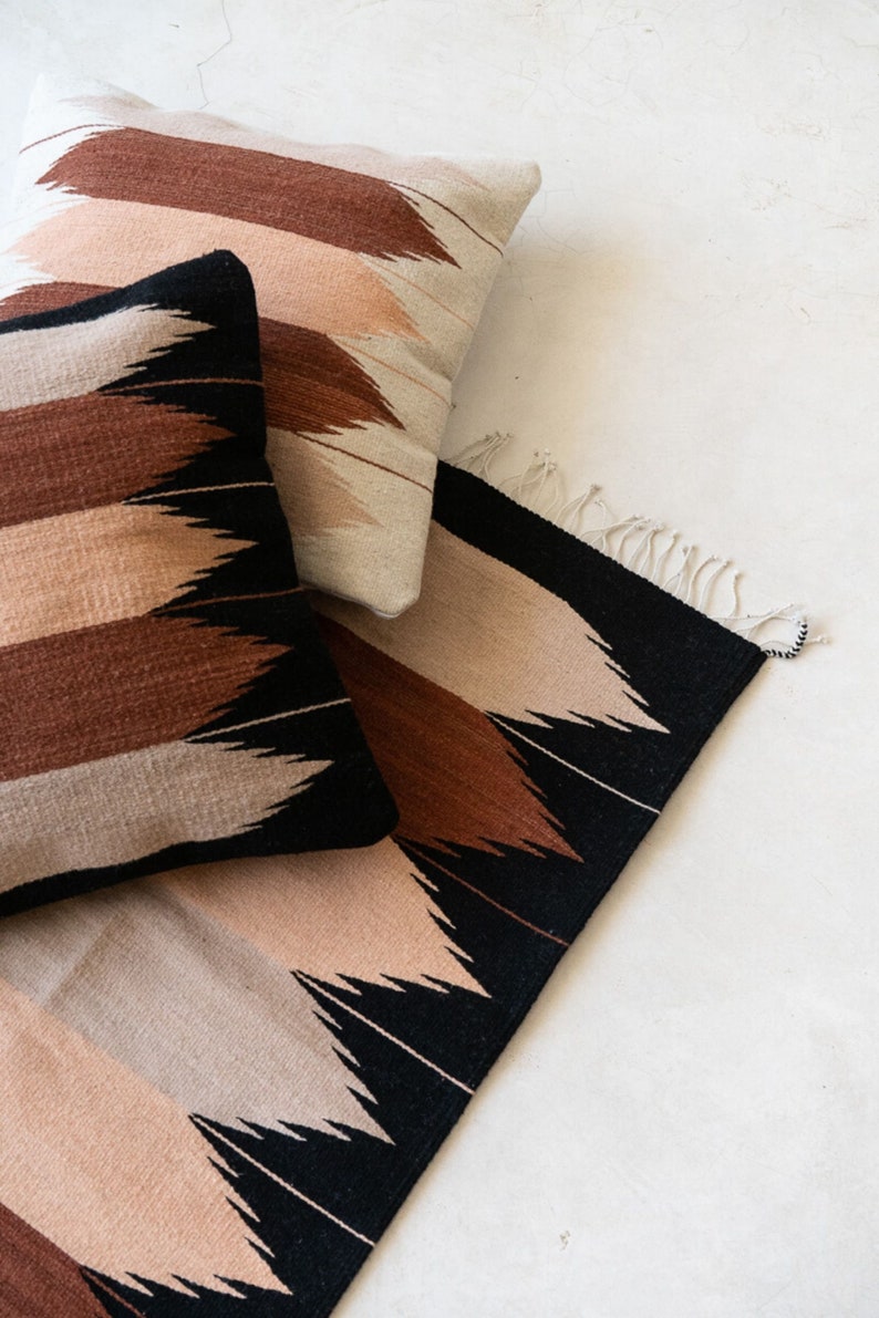May include: A set of three woven pillows and a rug with a geometric pattern in shades of brown, black, and beige. The pillows and rug have a fringe detail.