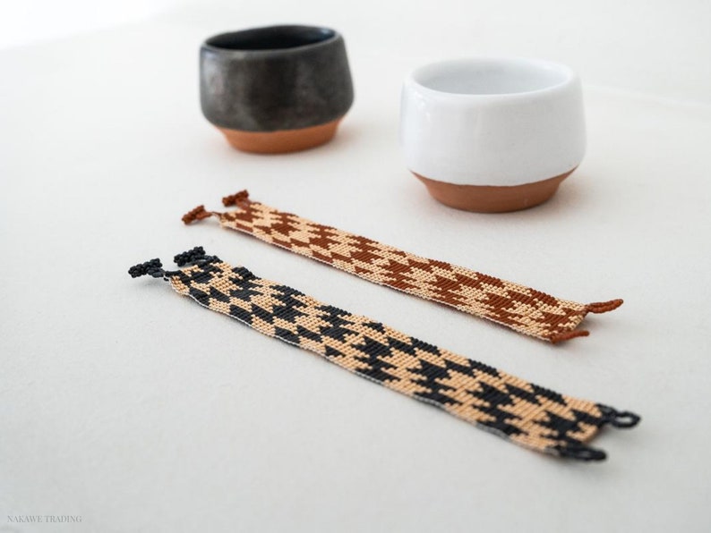 May include: Two woven bracelets with a houndstooth pattern. One bracelet is black and beige, and the other is brown and beige.