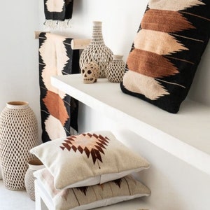 Puede incluir: Estantes blancos con una variedad de art&iacute;culos decorativos, incluyendo almohadas tejidas con patrones geom&eacute;tricos, jarrones de cer&aacute;mica y una calavera decorativa. Un sombrero de paja est&aacute; en el estante inferior.