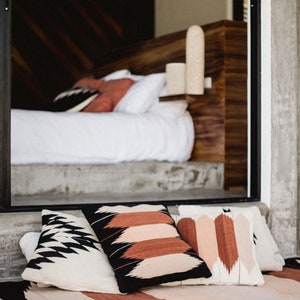 May include: A black and white patterned throw rug with three pillows. The pillows are black and white, brown and white, and pink and white. The rug has a fringe border.
