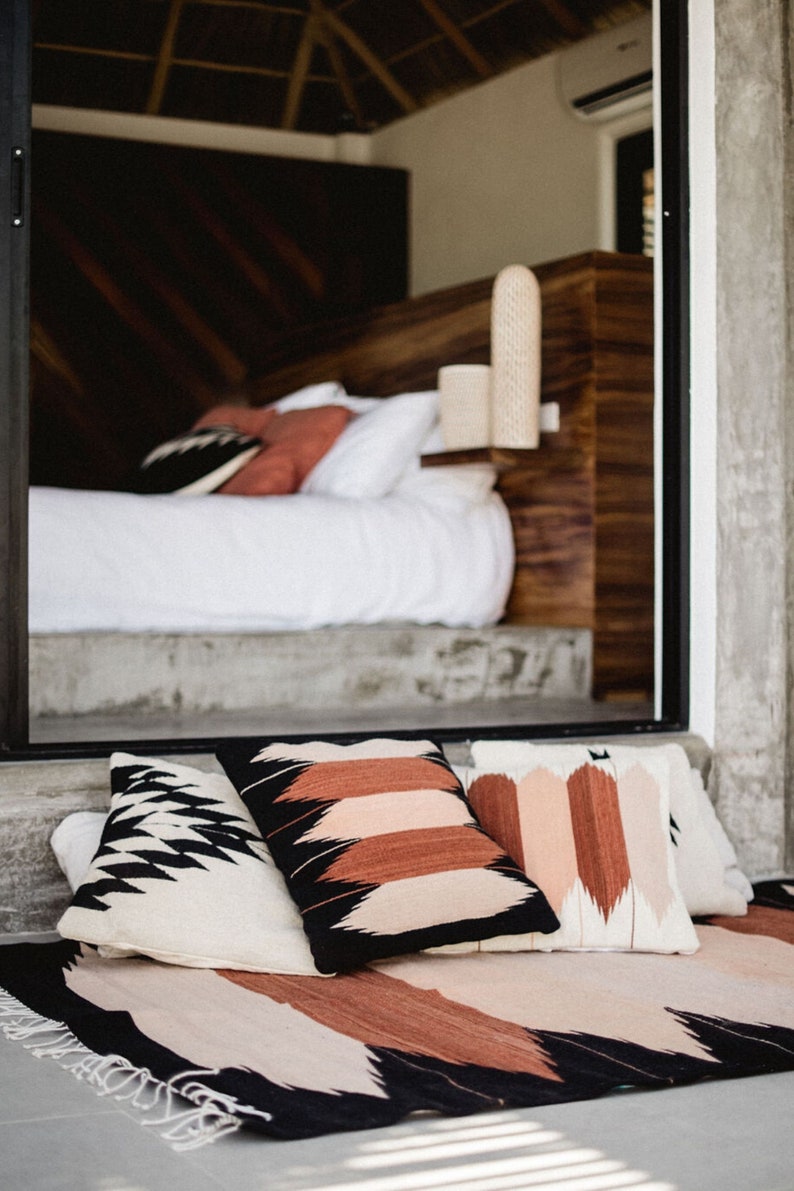May include: A black and white patterned throw rug with three pillows. The pillows are black and white, brown and white, and pink and white. The rug has a fringe border.
