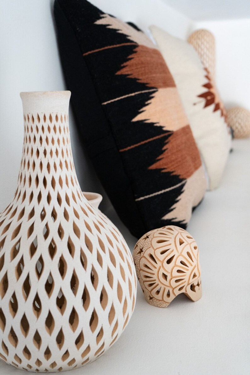 May include: Two white ceramic vases with intricate cut-out designs. One vase is tall and slender, the other is round and squat. Both vases have a light brown color.
