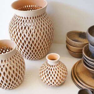 Op de afbeelding: Drie terracotta potten met een ruitvormig traliewerk. De potten zijn van verschillende grootte en zijn gerangschikt op een wit oppervlak.