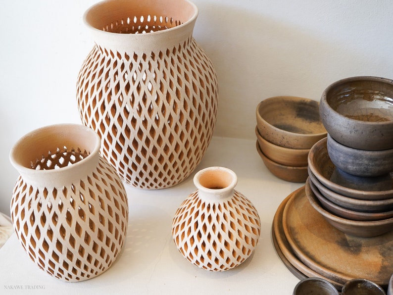 Op de afbeelding: Drie terracotta potten met een ruitvormig traliewerk. De potten zijn van verschillende grootte en zijn gerangschikt op een wit oppervlak.