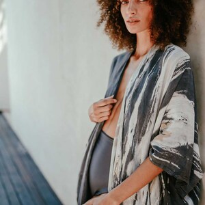 May include: A woman wearing a grey and white patterned kimono with a black swimsuit underneath. The kimono has a loose fit and is open at the front, revealing the swimsuit.