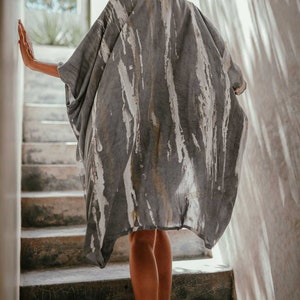 May include: A person wearing a grey and white tie-dye kimono-style top walking down a set of concrete stairs.