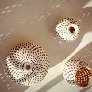 Op de afbeelding: Drie witte keramische vazen met ingewikkelde geometrische patronen in een lichtbruine kleur. De vazen zijn rond en hebben een brede opening aan de bovenkant.