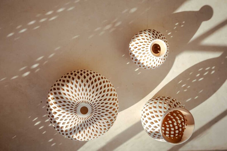 Op de afbeelding: Drie witte keramische vazen met ingewikkelde geometrische patronen in een lichtbruine kleur. De vazen zijn rond en hebben een brede opening aan de bovenkant.