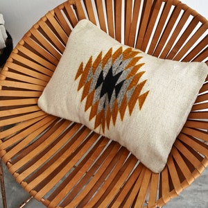 May include: A white pillow with a geometric pattern in shades of brown, gray, and black sits on a brown leather chair. The chair is made of woven leather strips and has a circular shape.