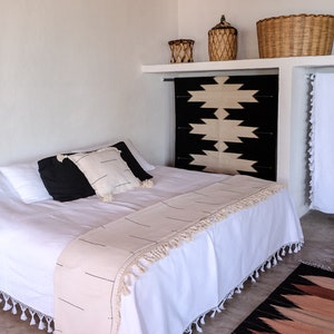 Puede incluir: Una cama blanca con una manta de tiro de patr&oacute;n blanco y negro y una alfombra de patr&oacute;n blanco y negro. La cama tiene una cabecera blanca y un piecero blanco. La habitaci&oacute;n est&aacute; decorada en un estilo minimalista.