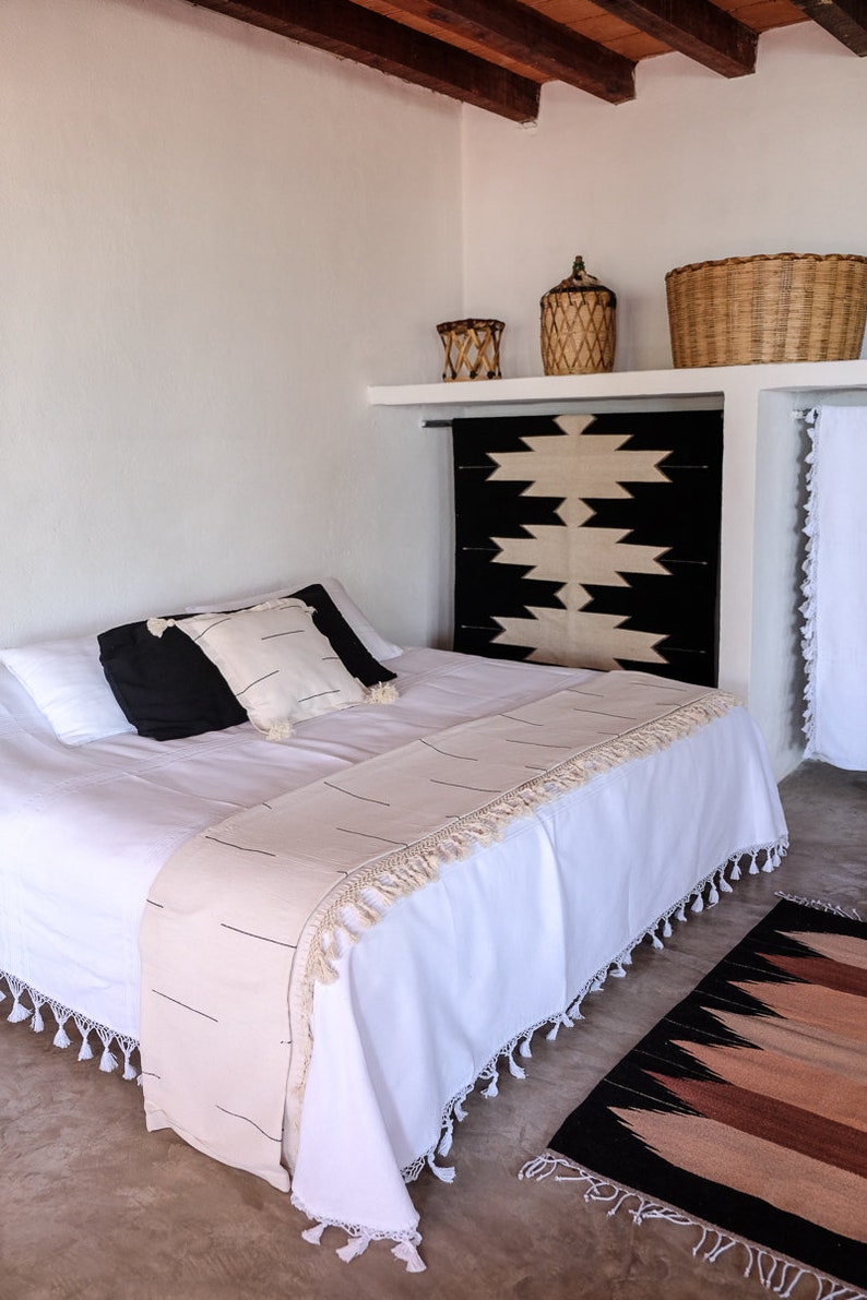 Puede incluir: Una cama blanca con una manta de tiro de patr&oacute;n blanco y negro y una alfombra de patr&oacute;n blanco y negro. La cama tiene una cabecera blanca y un piecero blanco. La habitaci&oacute;n est&aacute; decorada en un estilo minimalista.