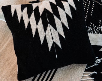 Puede incluir: Dos almohadas de tiro con patrones en blanco y negro con diseños geométricos. Las almohadas están hechas de tela tejida y tienen un borde de flecos.