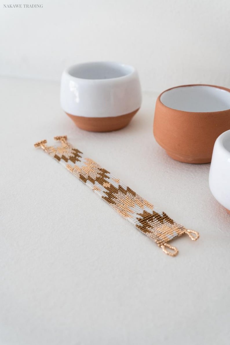May include: A white and brown beaded bracelet with a geometric pattern. The bracelet is made with small, evenly spaced beads and has gold-toned clasps.