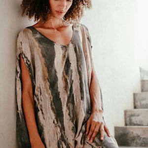 May include: A woman wearing a loose-fitting, sleeveless dress with a brown and grey abstract print. The dress has a scoop neck and a relaxed fit.