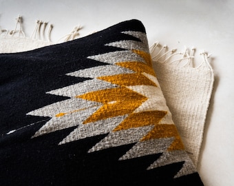 May include: A black, white, and mustard yellow throw pillow with a geometric pattern. The pillow is made of a soft, woven fabric.